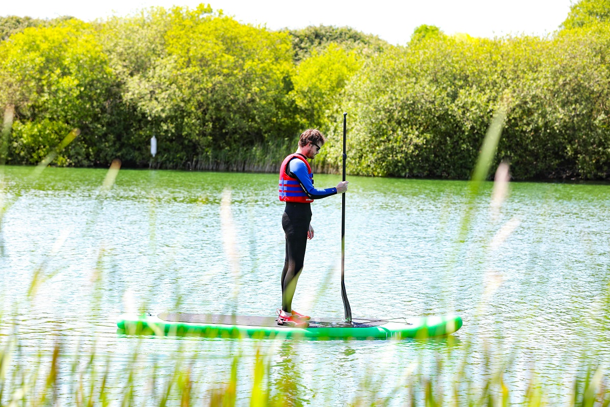 man in a life vest standing on a paddleboard at a river
